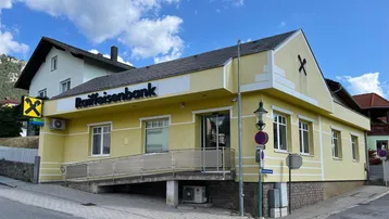 Gelbes Geschäftsgebäude mit Rampe und Raiffeisenbank-Beschriftung unter blauem Himmel.