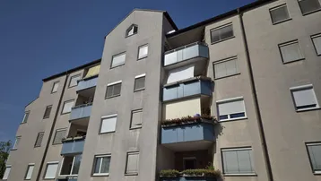 Mehrfamilienhaus mit mehreren Balkonen und blauen Akzenten unter klarem Himmel.