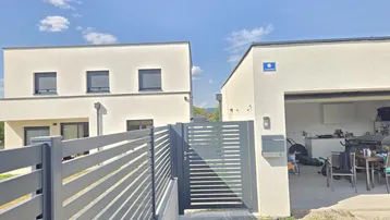 Moderne Häuser mit weißer Fassade, einem Zaun und einer offenen Garage unter blauem Himmel.