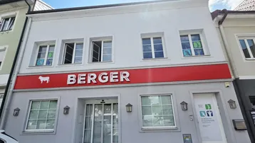 Fassade eines Geschäftsgebäudes mit rotem "BERGER"-Schild und mehreren Fenstern, die auf eine belebte Straße blicken.