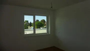 Leeres Zimmer mit Holzboden und Fenster mit Blick ins Grüne, ideal als Schlafzimmer.
