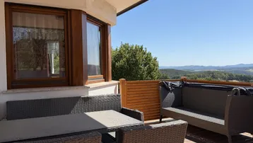 Möblierte Terrasse mit Rattanmöbeln und weitem Blick in die grüne, hügelige Landschaft.