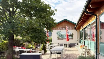 Geräumige Außenterrasse mit Tischen und Stühlen unter Bäumen, ideal für Mahlzeiten im Freien.