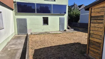 Rückseite des Hauses mit Solarpaneelen an der Fassade und einem trockenen Gartenbereich.