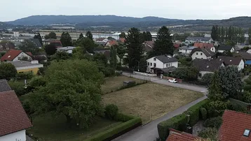 Weitläufige Luftaufnahme der Wohngegend mit Häusern, Grünflächen und fernen Hügeln.