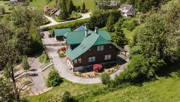 Luftaufnahme eines charmanten Hauses mit grünem Dach, umgeben von üppiger Natur und sanften Hügeln.