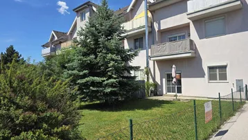 Mehrfamilienhaus mit gepflegter Fassade, Balkonen und einem grünen Gartenbereich unter blauem Himmel.