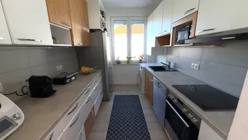 Moderne Einbauküche mit weißen und holzfarbenen Schränken, ausgestattet mit modernen Geräten und viel Tageslicht.