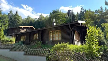 Blockhaus im Grünen mit Holzzaun und beeindruckendem Blick auf die umliegende Bergwelt.