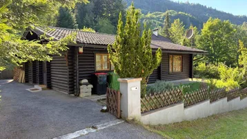 Rustikales Holzhaus im Blockhausstil mit Auffahrt und Blick auf die umliegende Berglandschaft.
