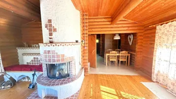 Gemütliches Wohnzimmer im Blockhaus mit großem Kamin, Holzboden und Blick auf den Essbereich.