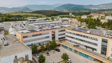Luftaufnahme eines modernen Büro- und Geschäftsgebäudes mit Solaranlagen auf dem Dach und umliegender Landschaft.