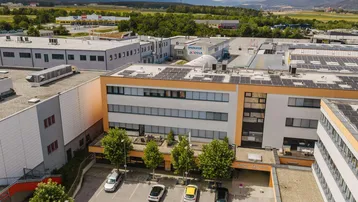 Luftaufnahme eines modernen Bürogebäudes mit Solaranlagen auf dem Dach und Parkplätzen davor.