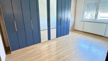 Schlafzimmer mit blauem Kleiderschrank, Spiegeltüren und hellem Laminatboden.