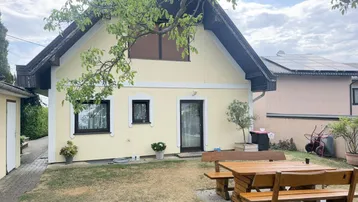 Rückseite des Hauses mit Garten, Sitzgelegenheit und Baumbestand.