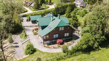 Luftaufnahme eines charmanten Chalets mit grünem Dach, umgeben von üppiger Natur und sanften Hügeln.