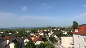 Weitläufiger Blick über eine ländliche Wohnsiedlung mit grünen Feldern und Bergen im Hintergrund.