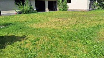 Große Rasenfläche vor einem langen Gebäude mit Garagentoren und einem angrenzenden Haus unter blauem Himmel.