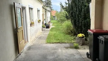Blick entlang der Hausfassade mit einem gepflasterten Weg und Grünflächen.