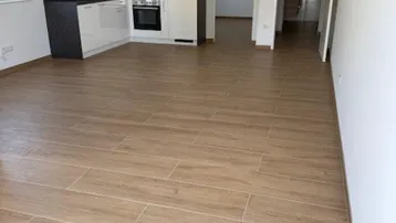 Heller, offener Wohnbereich mit integrierter Küche und modernem Fliesenboden in Holzoptik.