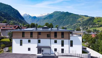 Modernes Mehrfamilienhaus mit Holzfassade und beeindruckendem Bergblick in grüner Umgebung.