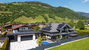 Modernes Einfamilienhaus mit Photovoltaikanlage, Garage und Pool in alpiner Landschaft.