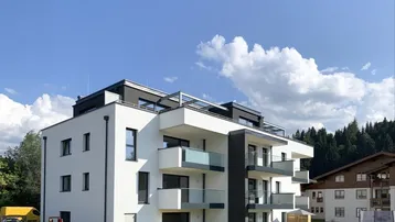 Modernes Mehrfamilienhaus mit weißer Fassade, Balkonen und einem kleinen Spielplatz im Grünen.