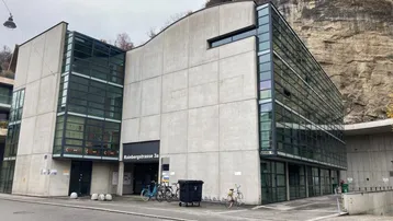 Modernes Gebäude mit Betonfassade und großen Glasflächen, direkt an einer Felswand gelegen.