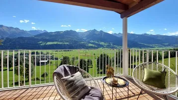 Geräumiger Balkon mit Holzboden, bequemen Sitzgelegenheiten und atemberaubendem Bergblick.
