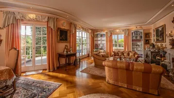 Elegantes Wohnzimmer mit Parkettboden, Stuckdecken und Zugang zu einem Balkon mit Gartenblick.