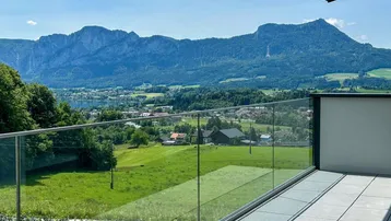 Geräumiger Balkon mit Glasgeländer und atemberaubendem Blick auf den See und die umliegende Berglandschaft.