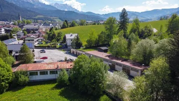 Luftaufnahme des Anwesens mit mehreren Gebäuden, Parkplätzen und umliegenden grünen Hügeln und Bergen.
