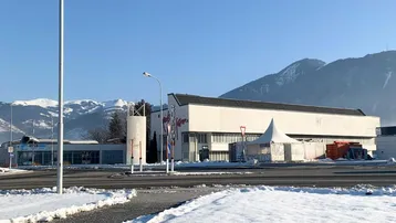 Gebäude mit weißer Fassade und dunklem Dach, umgeben von Schnee und Bergen im Hintergrund.