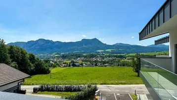 Panoramablick vom Balkon auf die umliegende Berglandschaft und grüne Wiesen unter blauem Himmel.