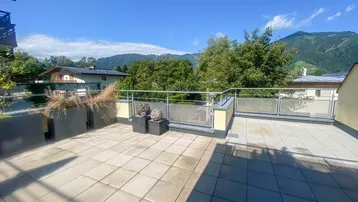 Große geflieste Terrasse mit Bergblick und grüner Umgebung unter blauem Himmel.