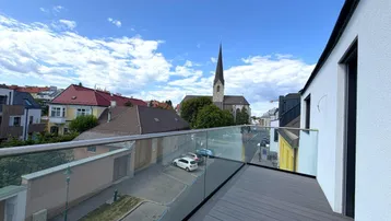 Blick von einem modernen Balkon mit Glasgeländer über die Straße und auf eine Kirche.