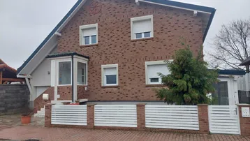 Einfamilienhaus mit Ziegelfassade, weißen Fensterläden und einem kleinen Vorgarten.