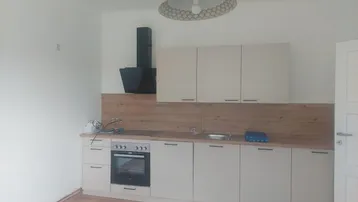 Neue Einbauküche mit hellen Schränken, Holzarbeitsplatte und integriertem Herd in einem frisch renovierten Raum.