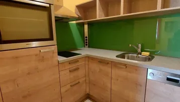 Kleine Küchenzeile mit Holzschränken, grünem Fliesenspiegel und integrierten Geräten.