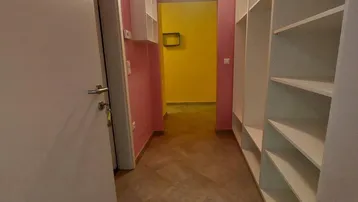 Langer Flur mit rosa Wänden und weißen Regalen, der zu einem gelben Raum führt.