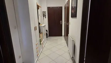 Langer Flur mit hellen Fliesen, dunklen Türen und einem weißen Garderobenschrank.