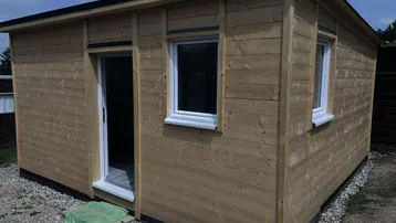 Kleines Holzhaus mit einfacher Holzfassade und Fenstern, umgeben von Schotter.