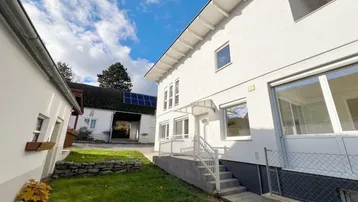 Seitenansicht des weißen Wohnhauses mit Treppe, Gartenbereich und Solarpaneelen auf dem Dach.