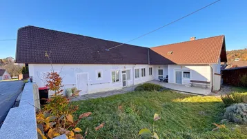 Ländliches Einfamilienhaus mit großem Vorgarten und Satteldach unter blauem Himmel.
