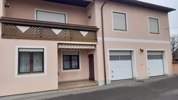 Vorderansicht des Hauses mit Balkon, Markise und zwei Garagen.