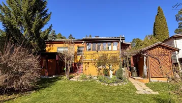 Hausfassade in warmem Gelb mit Garten und Terrasse unter blauem Himmel.