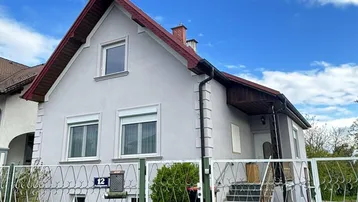 Vorderansicht eines Einfamilienhauses mit hellgrauer Fassade, rotem Satteldach und einem kleinen Vorgarten.
