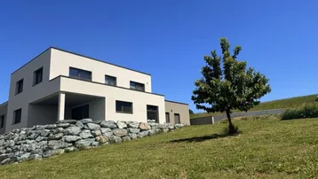 Modernes Einfamilienhaus mit heller Fassade und Steingarten auf einem grünen Hügel.