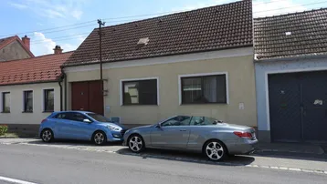 Vorderansicht eines Einfamilienhauses mit Satteldach und zwei geparkten Autos auf der Straße.