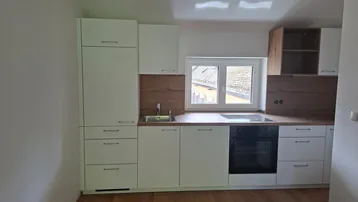 Helle Einbauküche mit weißen Schränken, Holzoptik-Arbeitsplatten und integrierten Geräten unter einem Fenster.